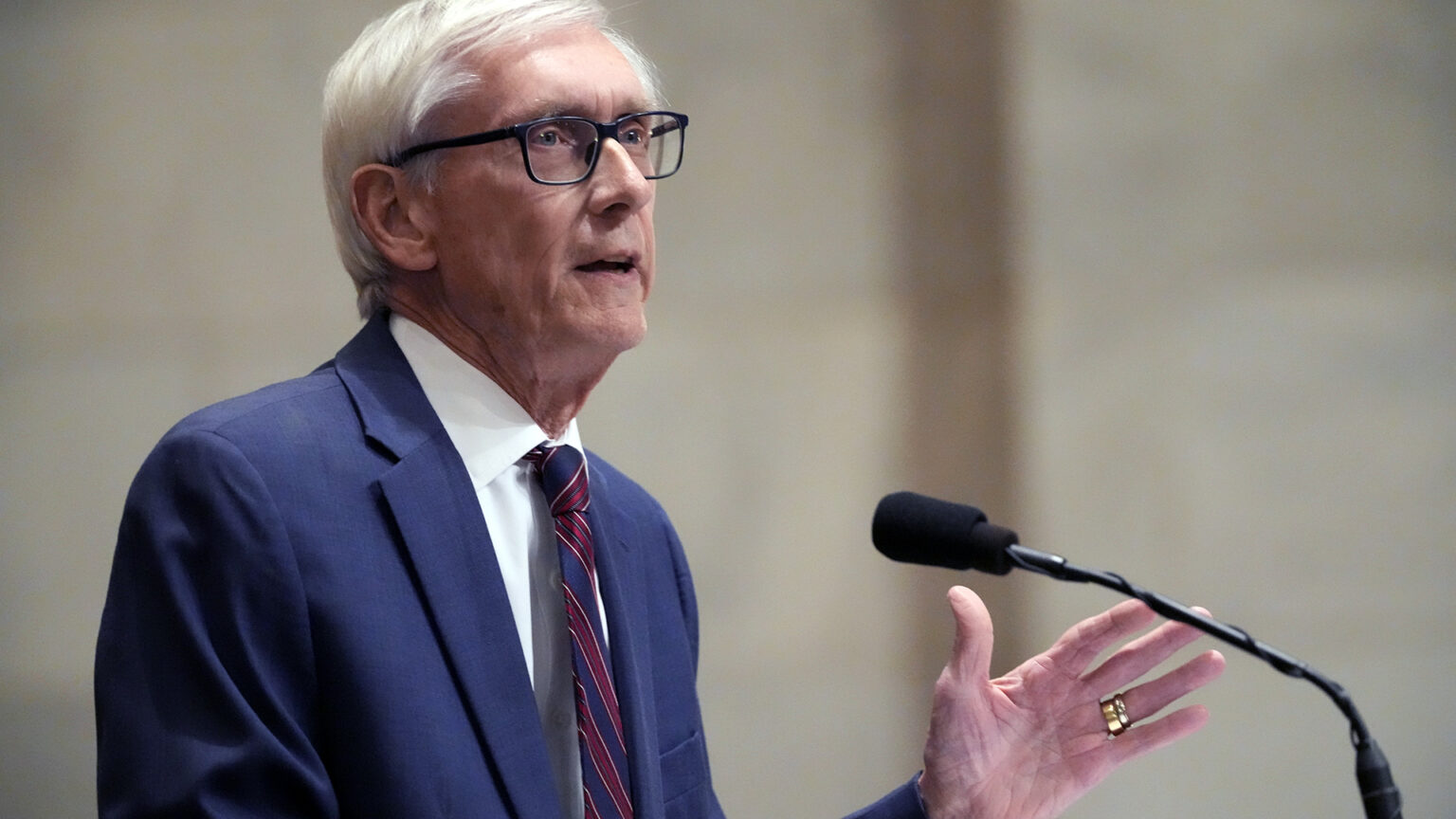 Tony Evers gestures with his left hand while speaking into a microphone.