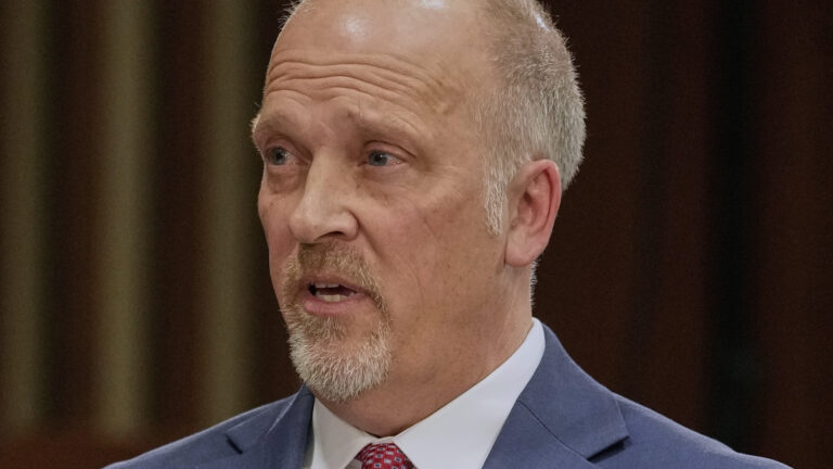 Brad Schimel speaks while sitting, with out-of-focus vertical wood slats in the background.