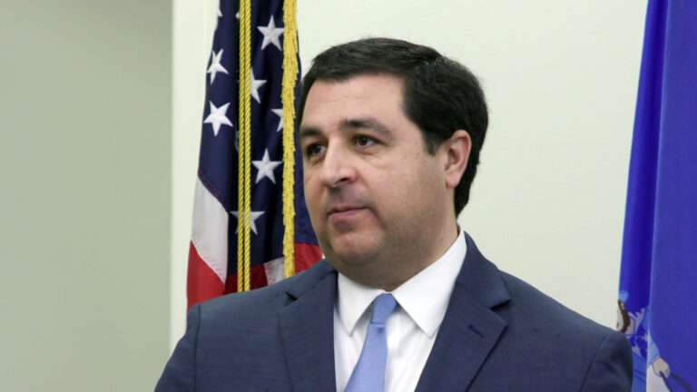 Josh Kaul speaks while standing in a room with the U.S. and Wisconsin flags displayed behind him.