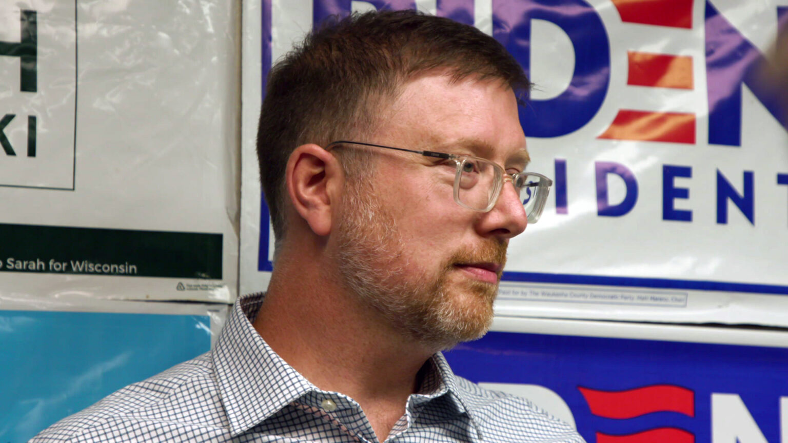 Ben Wikler speaks while standing in front of a backdrop of multiple political campaign yard signs.