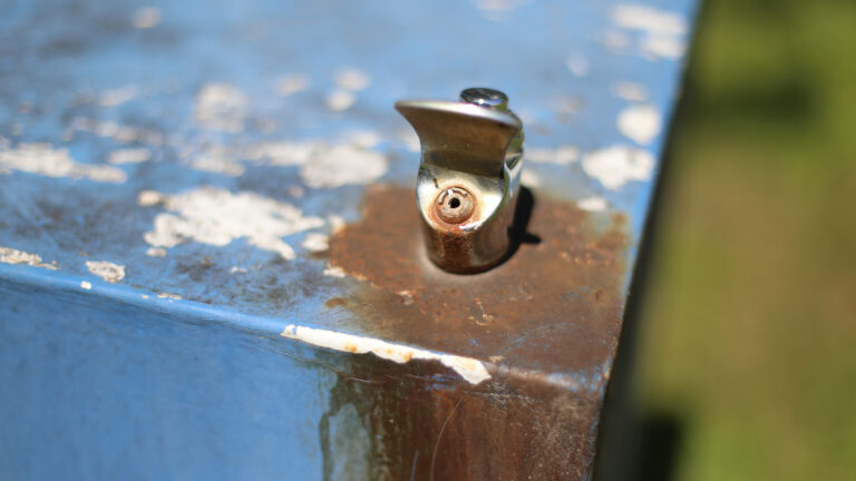 Rust covers and surrounds the spigot of a metal drinking fountain with chipped paint.