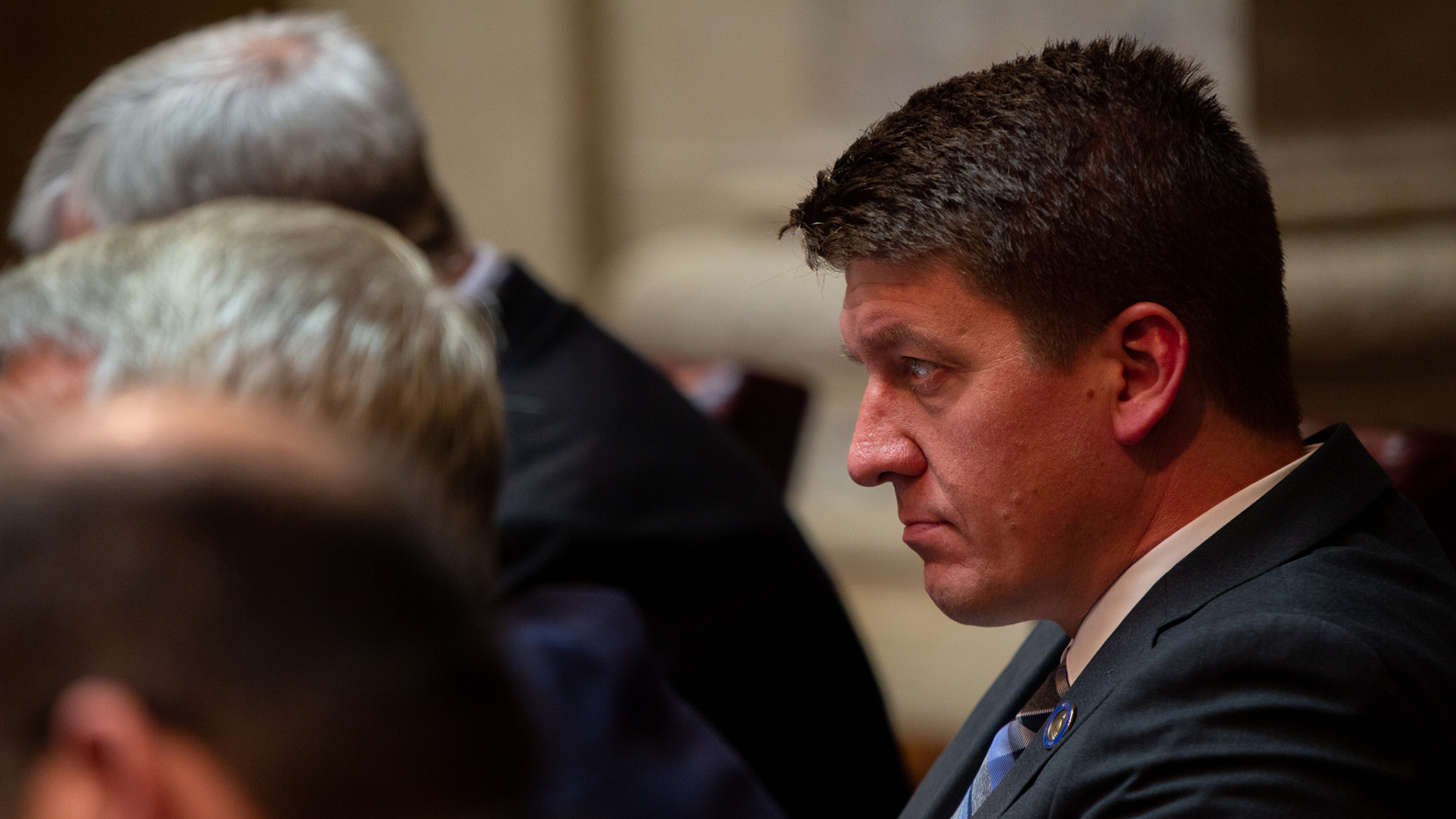 Eric Wimberger is seen in profile while seated behind a row of three other seated people.