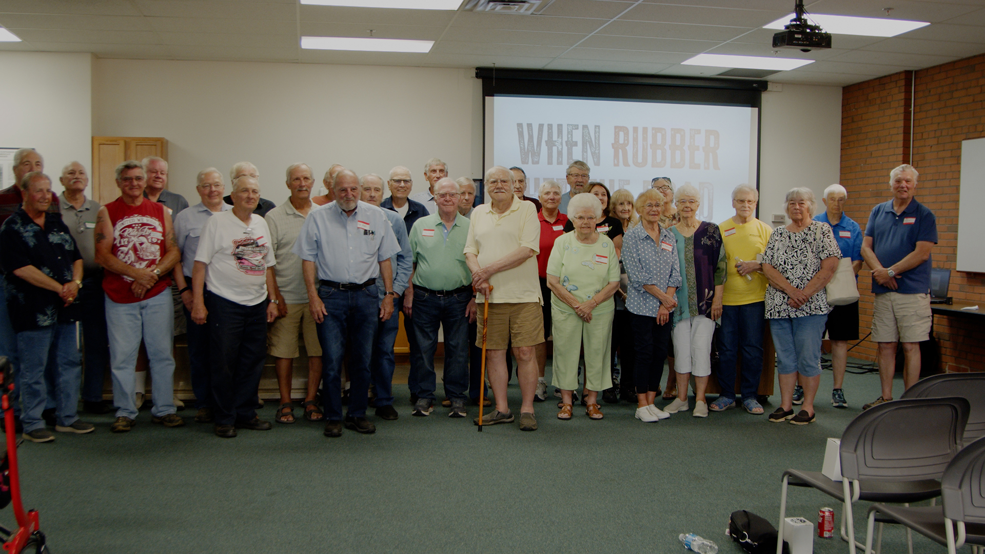 A group of individuals pose together inside of a conference room with a projector screen in the background.