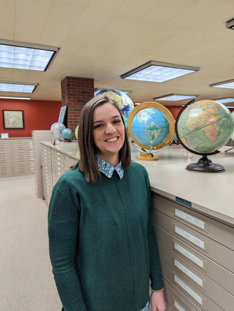 A woman smiles at the camera. There are several globes behind her.