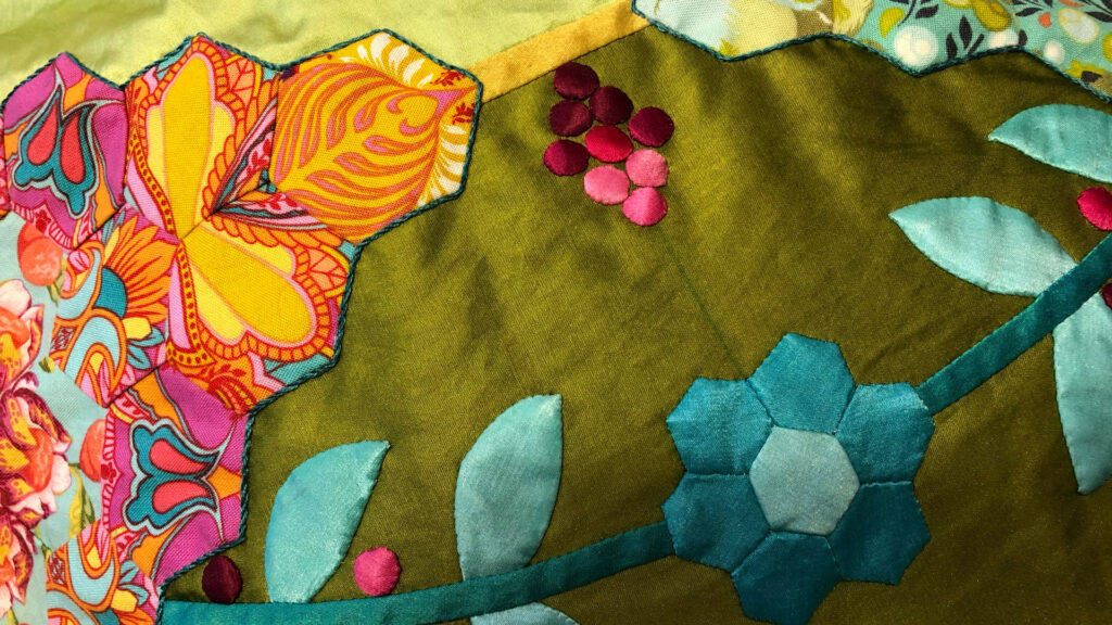 A close up of hexagons and vine details of a green, turquoise and pink quilt. 
