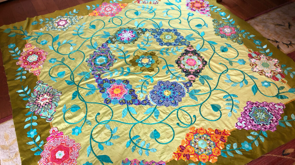 An in-progress look at an intricate quilt celebrating hexagons in greens, turquoises, pinks, purples and oranges. 