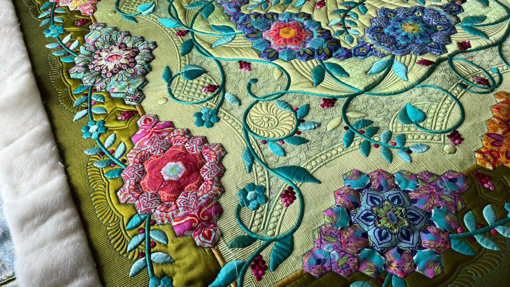 A intricate quilt celebrating hexagons in greens, turquoises, pinks, purples and oranges next to batting.