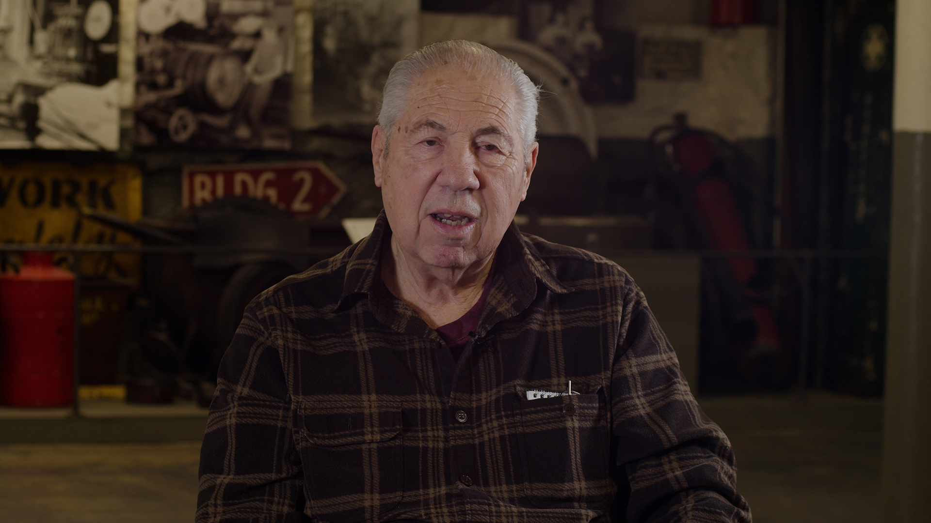 A man speaks to the camera in front of a collage of images from the Uniroyal tire plant.
