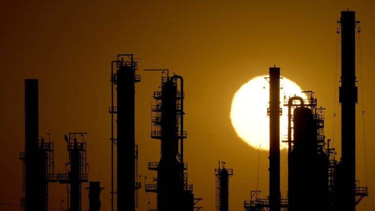 Multiple industrial towers with scaffolding, pipes and other exterior elements are shadowed from behind by the sun, with heat shimmering the edges of its light. Multiple industrial towers with scaffolding, pipes and other exterior elements are shadowed from behind by the sun, with heat shimmering the edges of its light.