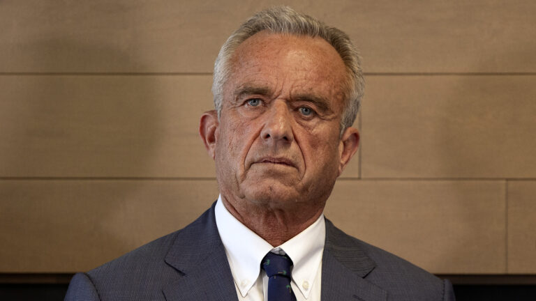 Robert F. Kennedy Jr. listens while standing in front of a wood-paneled wall.