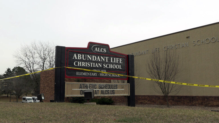 Plastic tape marked multiple times with the words Sheriff's Line Do Not Cross is attached to a wood sign with the words Abundant Life Christian School, Since 1978, Elementary - High School and a wordmark reading ALCS above a marquee-style letter sign with the words Athletic Schedules Online At alcs.us, which stands on a lawn and multiple leafless trees in front of a multi-story building with a stucco exterior and a letter sign reading Abundant Life Christian School, with parked vehicles and more trees in the background. Plastic tape marked multiple times with the words Sheriff's Line Do Not Cross is attached to a wood sign with the words Abundant Life Christian School, Since 1978, Elementary - High School and a wordmark reading ALCS above a marquee-style letter sign with the words Athletic Schedules Online At alcs.us, which stands on a lawn and multiple leafless trees in front of a multi-story building with a stucco exterior and a letter sign reading Abundant Life Christian School, with parked vehicles and more trees in the background.