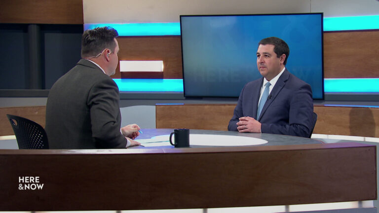 Zac Schultz and Josh Kaul sit facing each other on the Here & Now set.