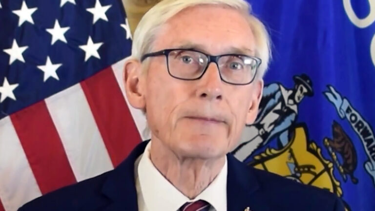 Tony Evers speaks while standing in front of a U.S. and Wisconsin flag.