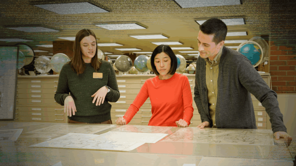 Three people stand over a map spread out on a table