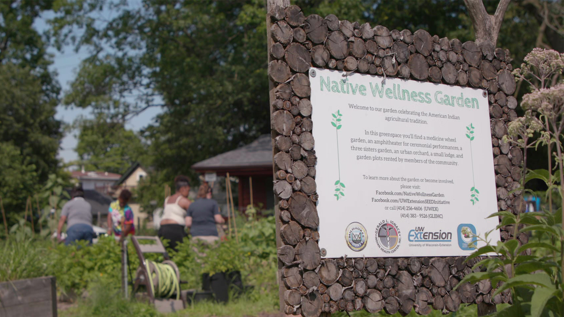 A “Native Wellness Garden” sign is displayed with a group of people gathered nearby, engaging with the natural environment.