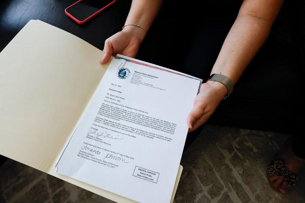 Hands holding a Madison Police Department clearance letter for Miguel Jose Robles, dated May 27, 2025.
