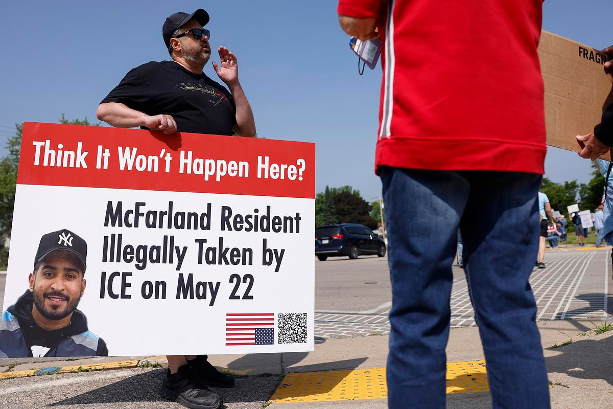 “Man at a protest holding a sign reading ‘Think It Won’t Happen Here? McFarland Resident Illegally Taken by ICE on May 22’ with photo of a man in a Yankees cap.”