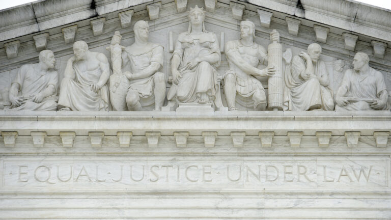 A pedimental frieze showing statues of seven figures seated above the words Equal Justice Under Law is carved in a marble masonry building.