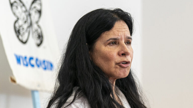 Christine Neumann-Ortiz sits and speaks in a room with an out-of-focus print on the wall in the background.