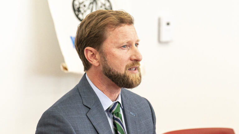Cain Oulahan sits and speaks in a room with an out-of-focus print on the wall in the background.