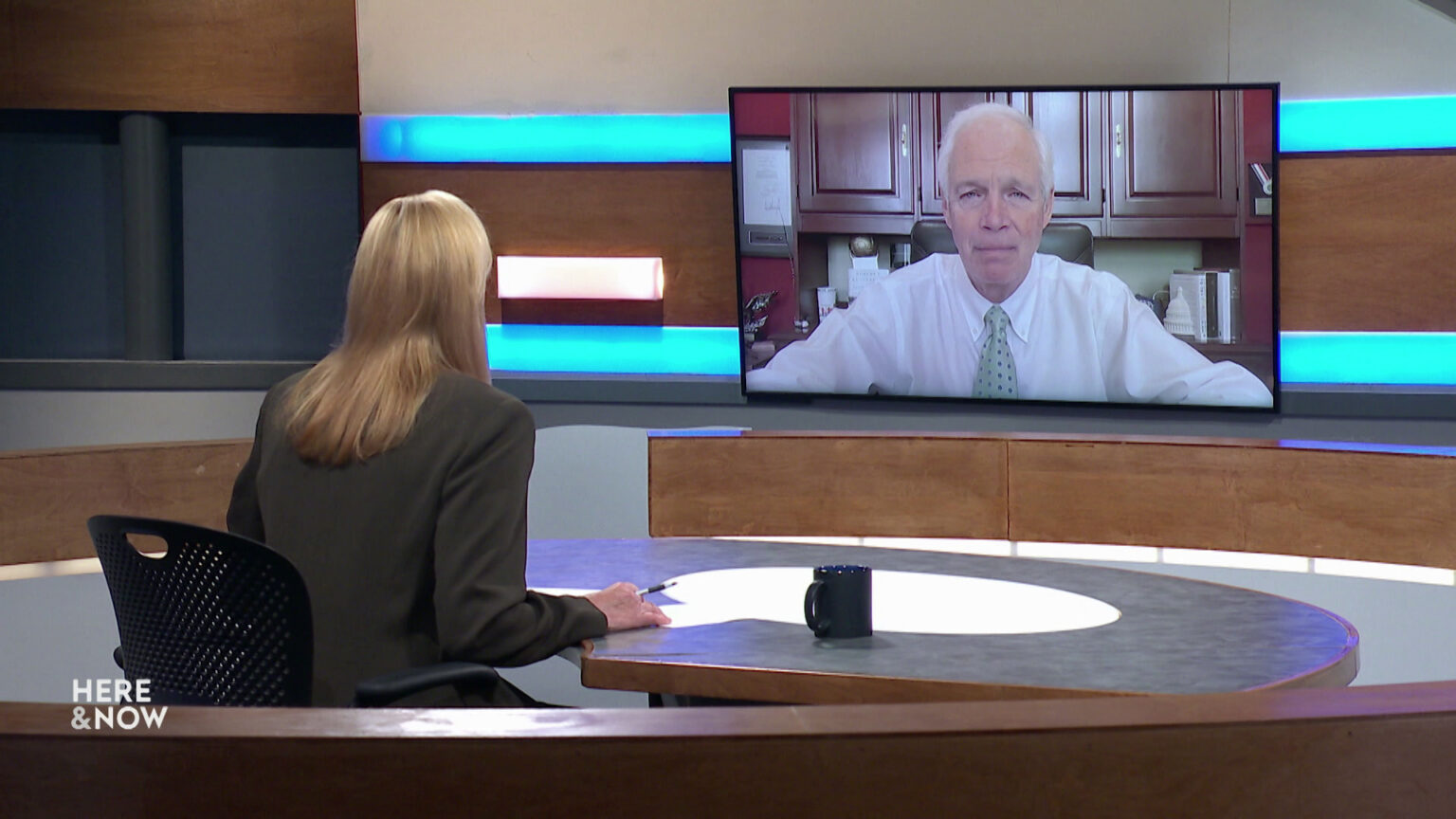 Frederica Freyberg sits at a desk on the Here & Now set and faces a video monitor showing an image of Ron Johnson. Frederica Freyberg sits at a desk on the Here & Now set and faces a video monitor showing an image of Ron Johnson.
