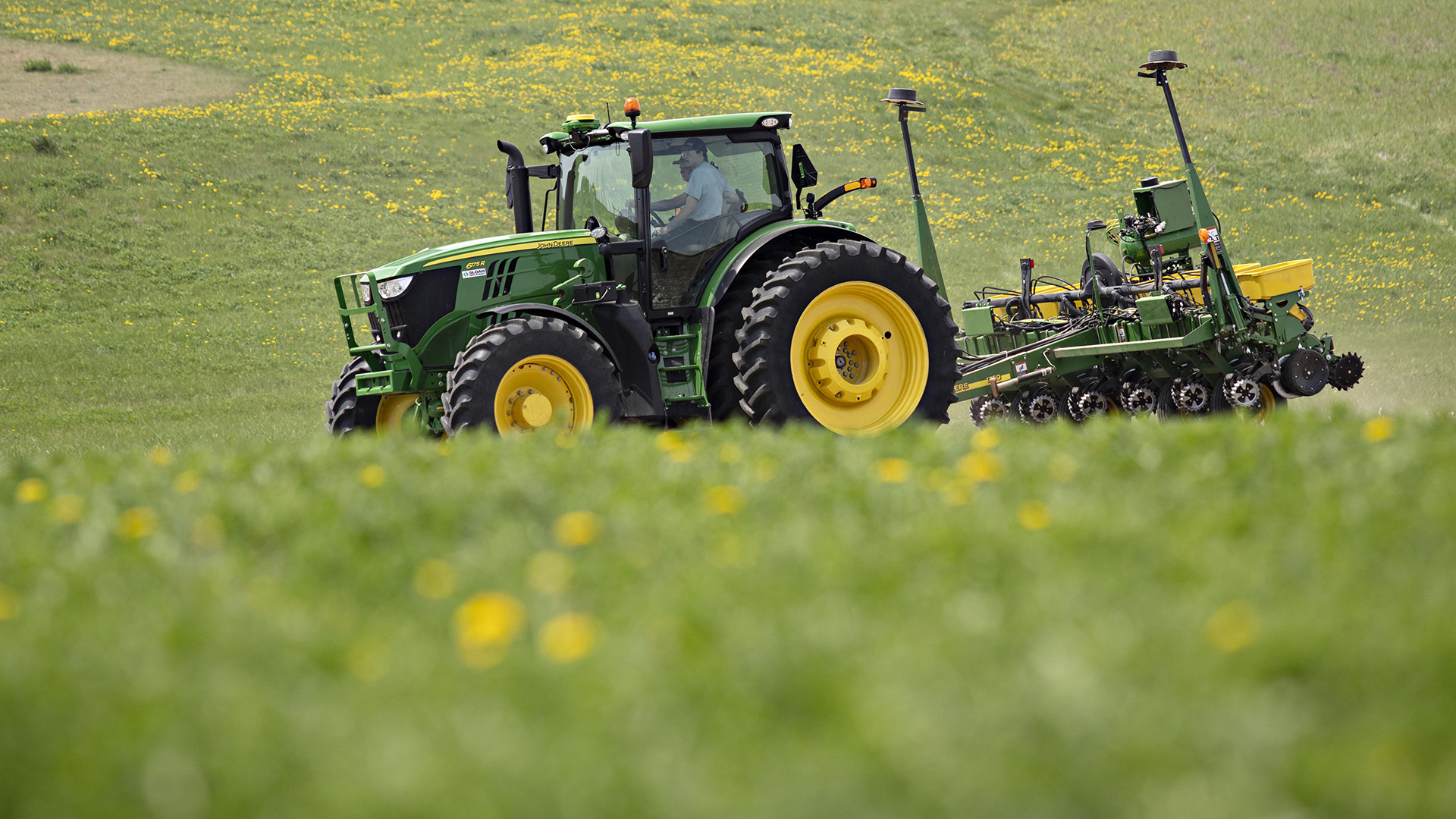 Jamin Crapp sits in the cab of a tractor pulling a planter over a field, with an out-of-focus hillside in the foreground.