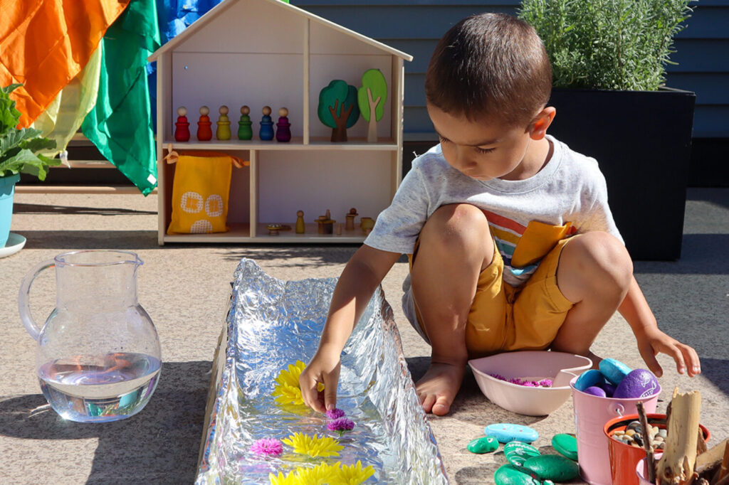 A child plays in a pretend river made from cardboard and foil.