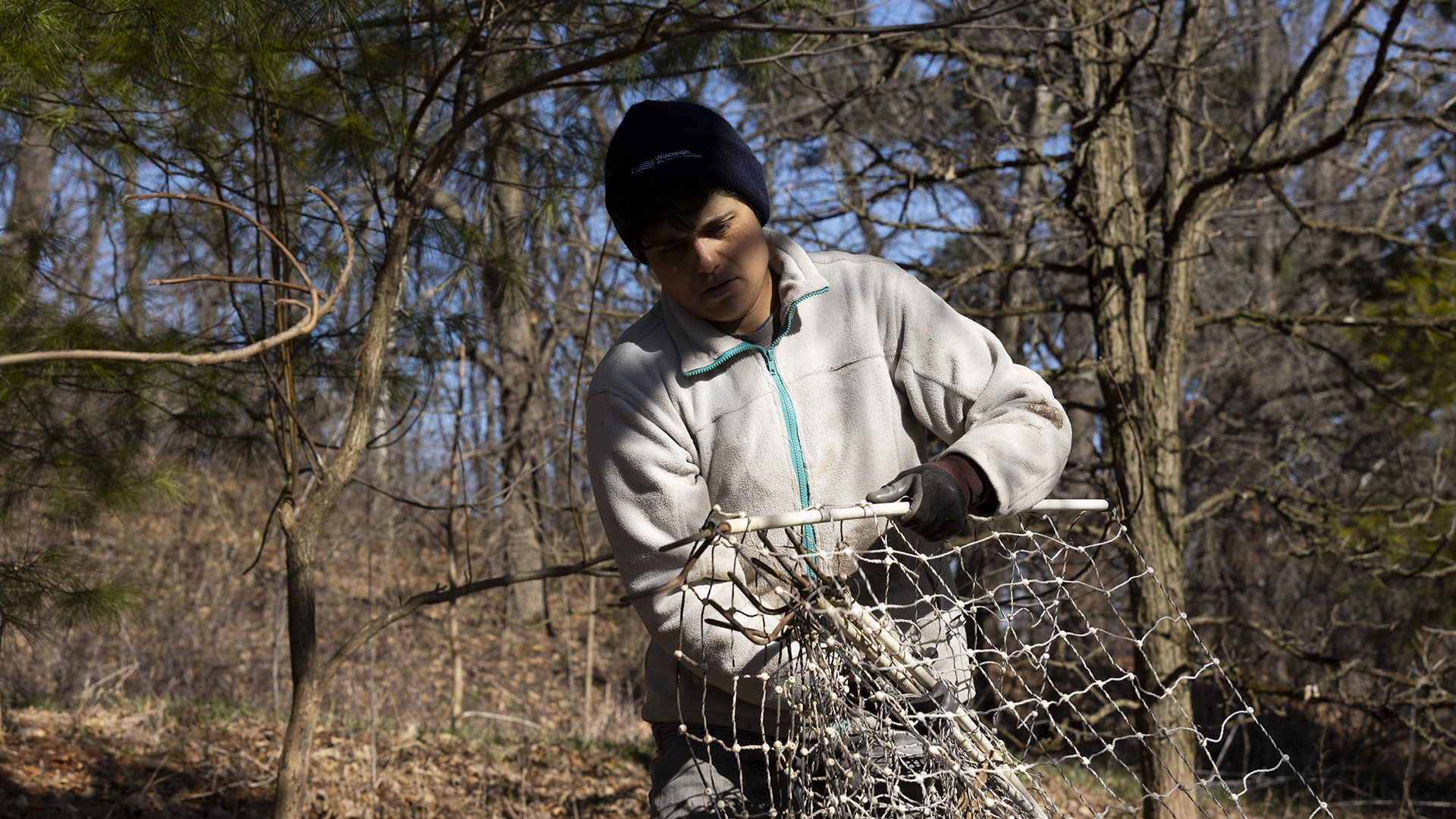 Jess D'Souza handles fencing while standing in front of multiple leafless trees.