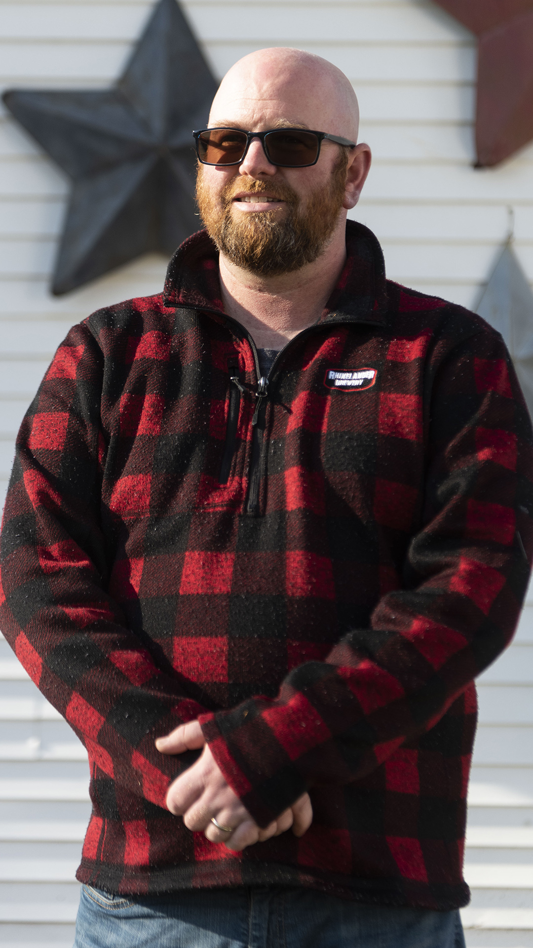 Rohn Bishop poses for a photo with his hands folded in front of him while standing in front of a wall with siding panels and decorative stars.