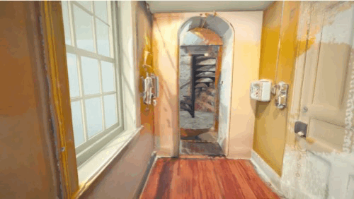 Narrow hallway with wooden floor leading to an archway and spiral staircase.