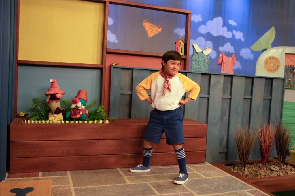 A boy poses next to two garden gnome puppets on a television set.