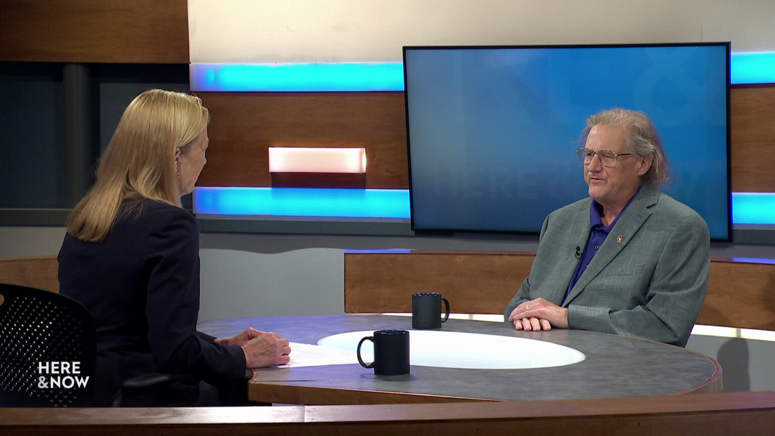 Frederica Freyberg and Steven Deller sit facing each other on the Here & Now set.