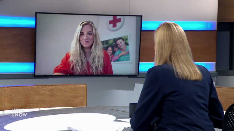 Frederica Freyberg sits at a desk on the Here & Now set and faces a video monitor showing an image of Kathryn Halvorsen.