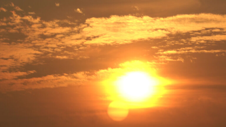 The sun and adjacent clouds are obscured and tinted by hazy air.