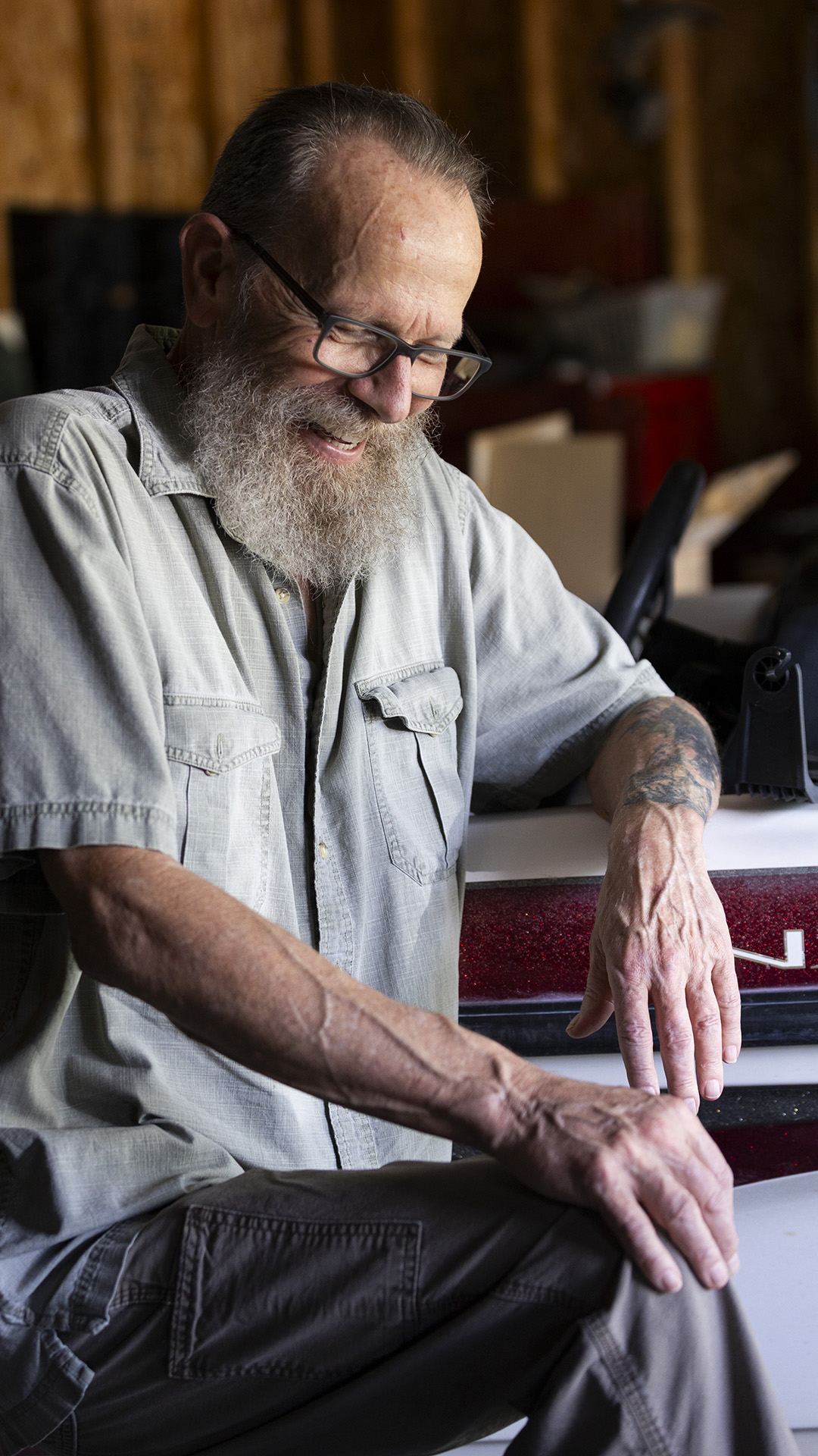 Earl Lowrie smiles while seated next to a boat parked inside a garage with plywood walls.