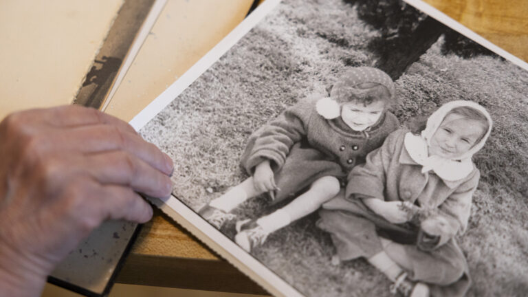 A right hand holds the corner of a black and white photo of Dorothy Thompson as a child seated next to another child on a lawn.