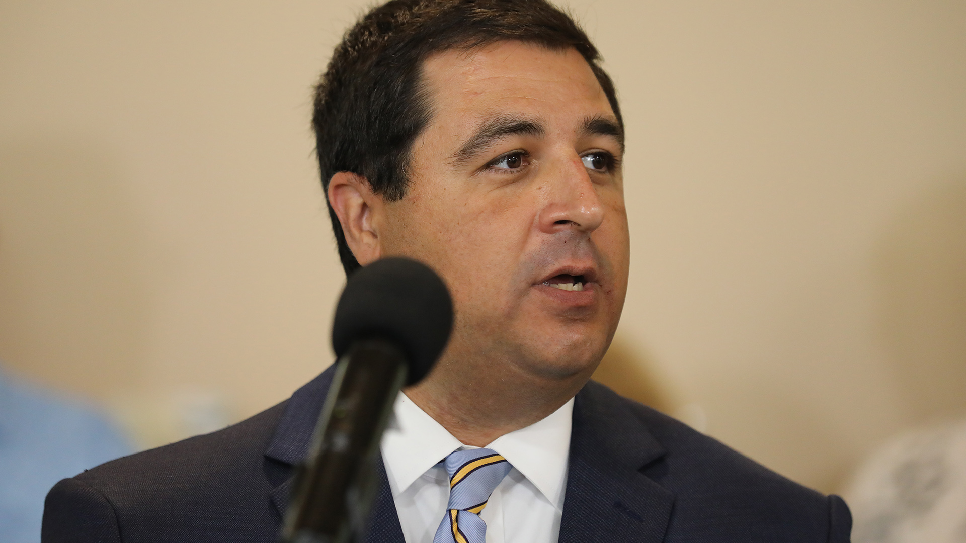 Josh Kaul speaks while standing in front of an out-of-focus microphone.