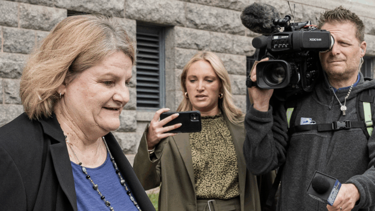 Milwaukee County Circuit Judge Hannah Dugan walks outside a stone building while surrounded by reporters. A cameraman films, a woman holds up a phone.