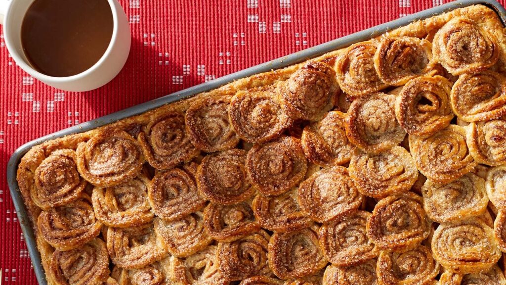 A glamor shot of a cinnamon swirl sheet pan bake next to a cup of coffee.