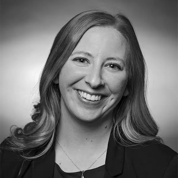 Black-and-white portrait of a smiling woman with long wavy hair, wearing a blazer and necklace.