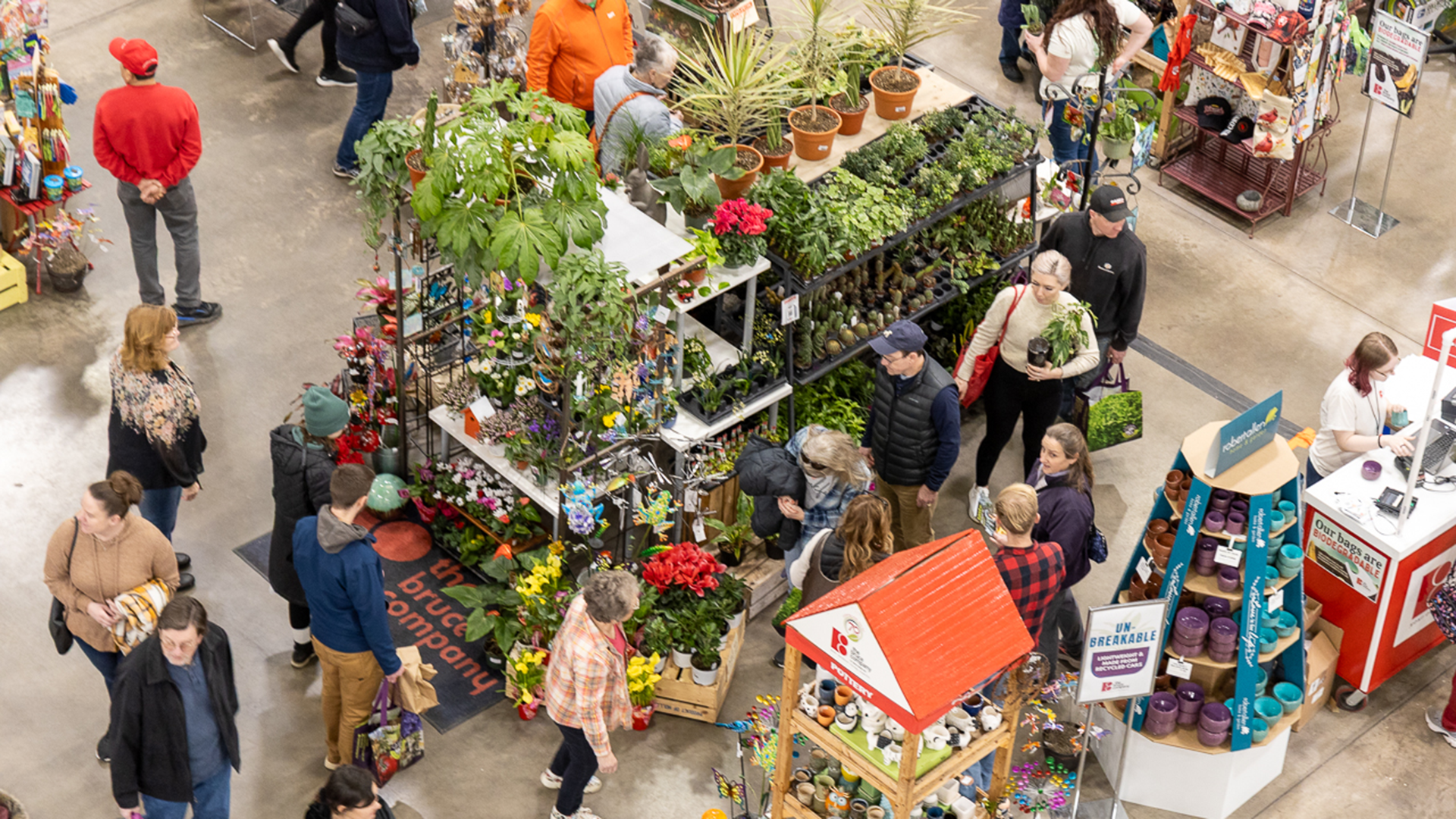 Overhead view of shoppers browsing colorful plants and garden supplies at an indoor expo.