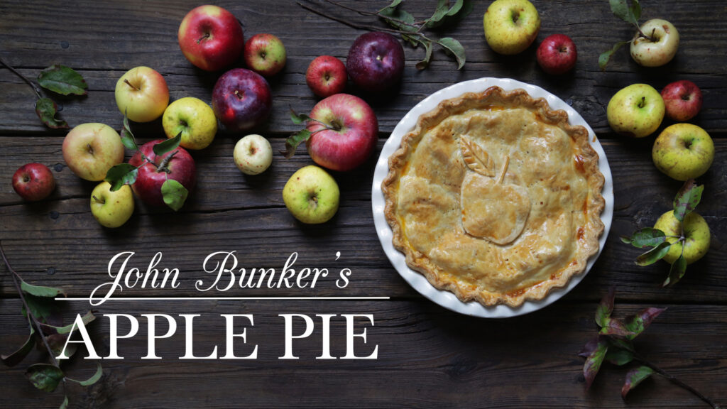 A glamor shot of a decorative apple pie, surrounded by apples, and a logo, "John Bunker's Apple Pie" next to it.