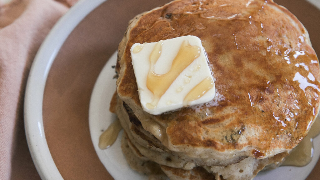 A close up glamor shot of a stack of pancakes, complete with butter and syrup.