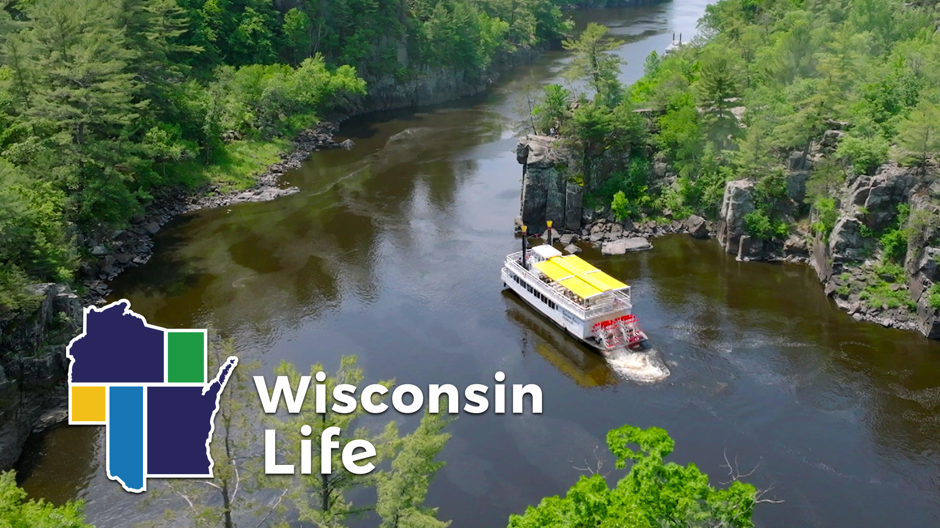 A white riverboat with a yellow canopy travels along a wooded river gorge, with "Wisconsin Life" and a Wisconsin map graphic in the lower left corner.