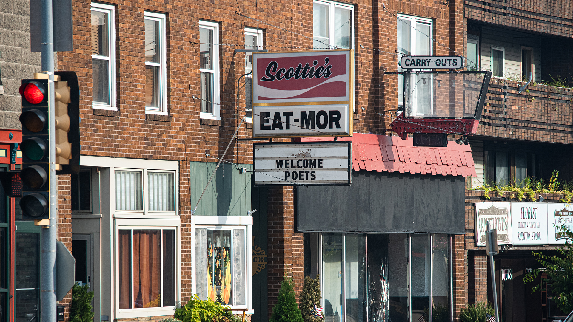 A red brick building featuring a sign reading 'Welcome Poets' in front of a traditional facade and prominent entrance.