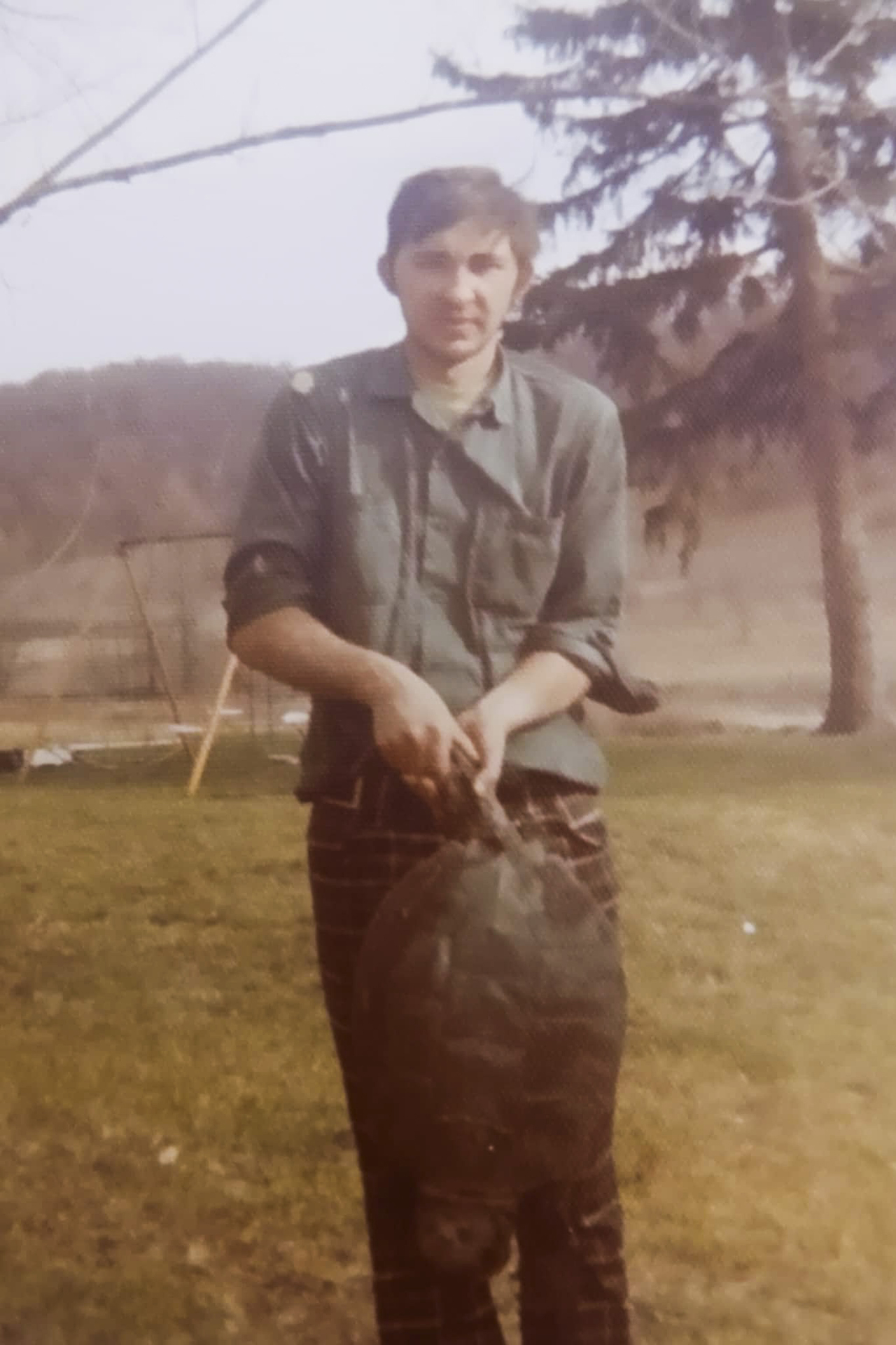 A vintage photo shows Jimmy Novy holding a large turtle in both hands while standing outside with a tree and hillsides in the background.