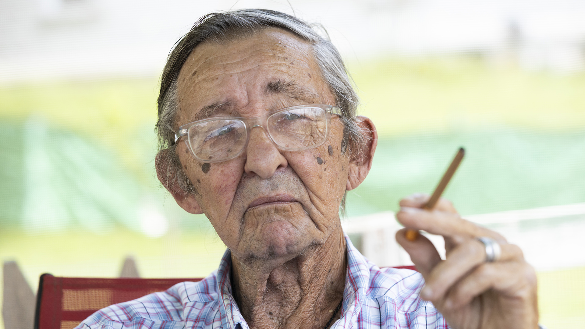 Jimmy Novy poses for a portrait while seated and holding a cigar in his out-of-focus left hand.