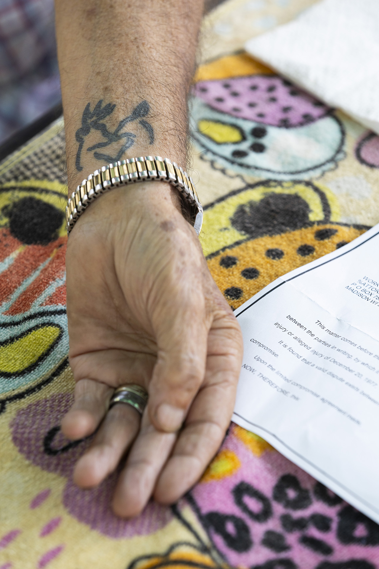 Jimmy Novy displays a tattoo of a stylized buck on his left wrist while resting his hand face up on top of a towel and next to a sheet of paper that are on the surface of a table while wearing a ring and metal watch.