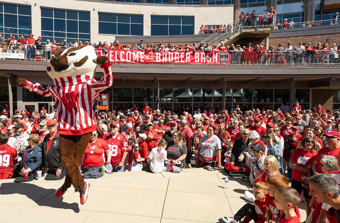 Cecil Powless as the Bucky Badger mascot dressed in a red and white striped shirt with a motion W stands proudly in front of an enthusiastic crowd, promoting excitement at the Badger Bash in Union South.