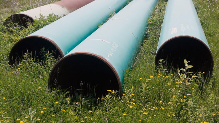 Multiple disconnected segments of a metal pipeline sit on an open field. Multiple disconnected segments of a metal pipeline sit on an open field.